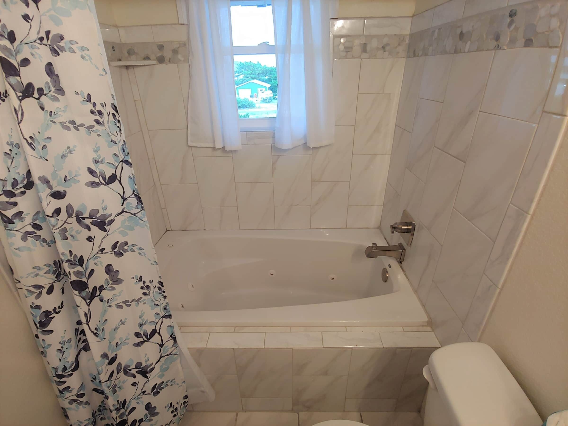 Ein Badezimmer mit einer Badewanne, einer Toilette und einem Fenster mit Blick auf Grünflächen.