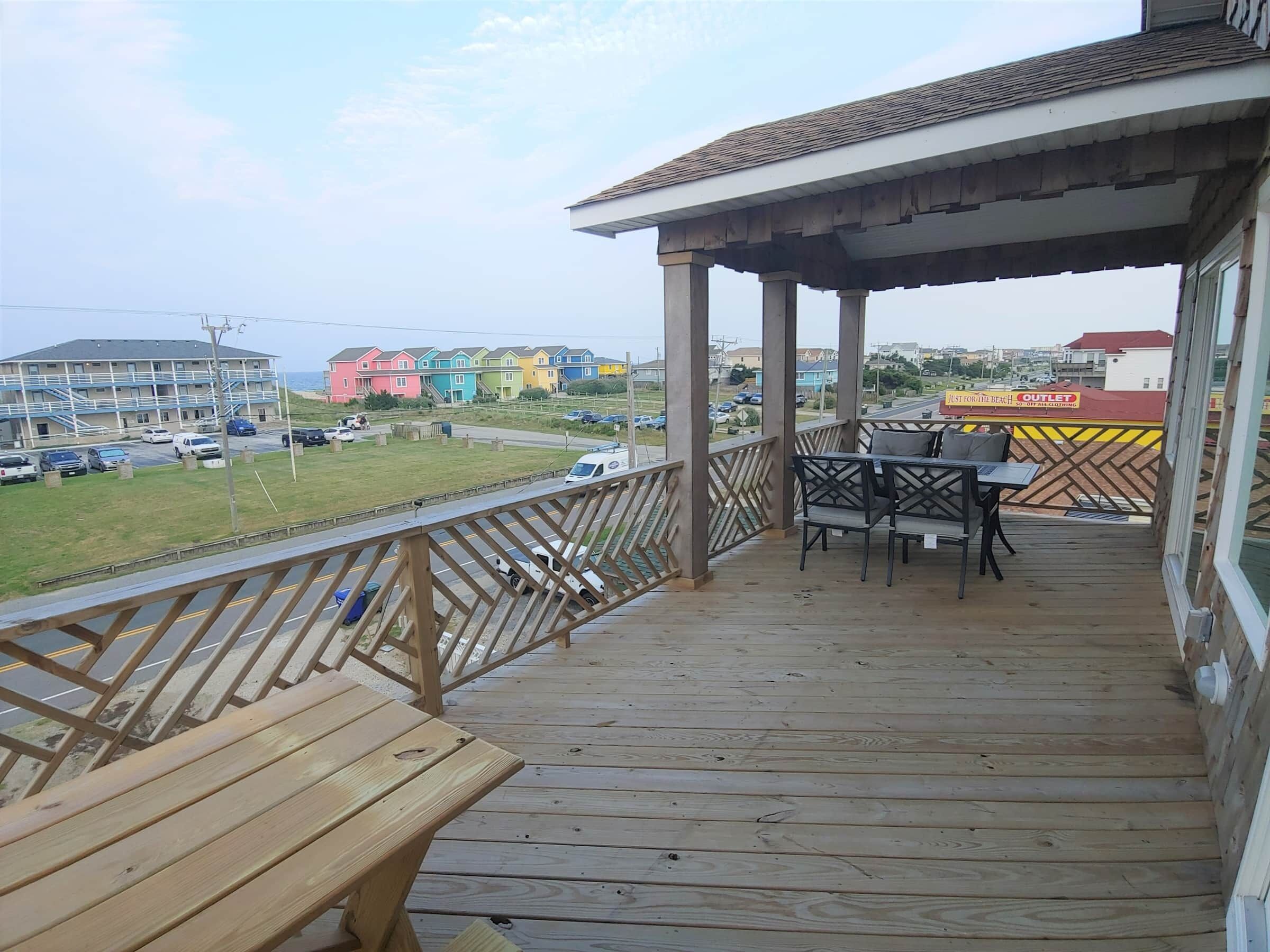 A wooden deck with a table and chairs, overlooking a parking area and colorful buildings.