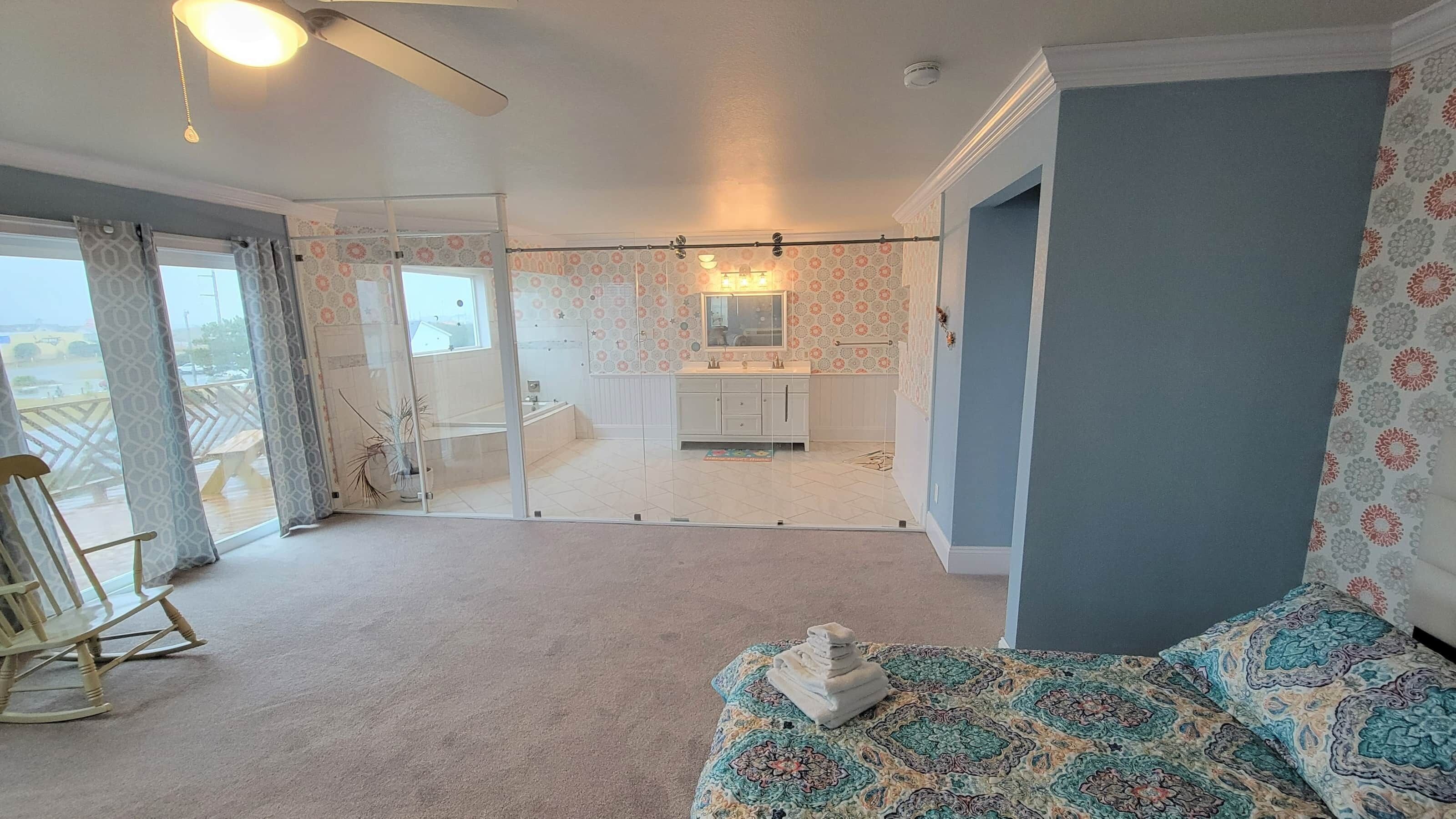 A bedroom with a bed, a rocking chair, a bathroom with a sink and mirror, and a balcony with a view.