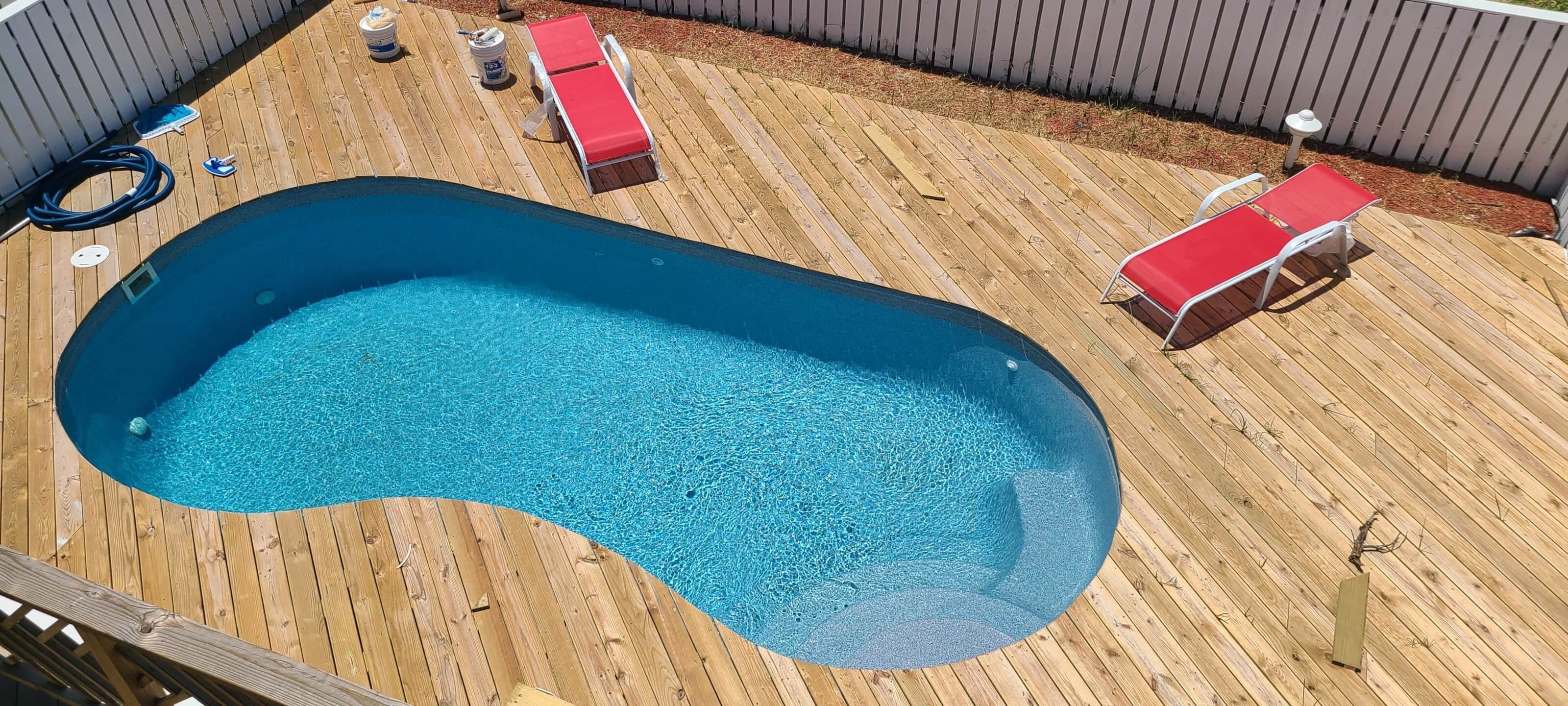 A swimming pool with two red lounge chairs and a hose on a wooden deck.