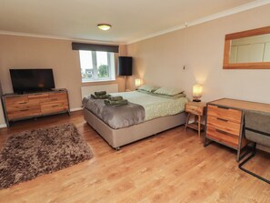 A bedroom with a bed, a desk, a television, and a window.