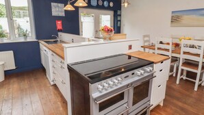 A kitchen with a stove, oven, and dining area with chairs and a table. - Asta Cottage (Morpeth)
