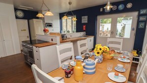 A kitchen with white cabinets, a stove, and a dining table set with plates, glasses, and a vase of sunflowers. - Asta Cottage (Morpeth)