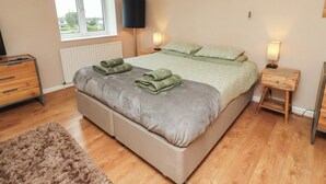 A bedroom with a bed, two bedside tables, a TV, a radiator, and a window. - Asta Cottage (Morpeth)