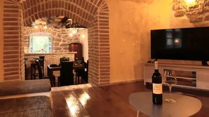 A cozy living room with a stone archway leading to a dining area, a flat-screen TV, and a bottle of wine on a table. - Beautiful 3-bed House in Kotli (Buzet)