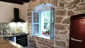 A kitchen with a stone wall, a window with flowers, a stove, and a red refrigerator. - Beautiful 3-bed House in Kotli (Buzet)