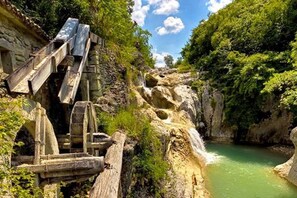 A rustic stone bridge over a river, surrounded by lush greenery and a clear sky.