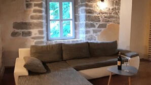 A cozy living room with a stone wall, a large window, a sofa, a coffee table, and a bottle of wine. - Beautiful 3-bed House in Kotli (Buzet)