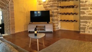 A cozy living room with a stone wall, a flat-screen TV, a wine bottle, and a small table. - Beautiful 3-bed House in Kotli (Buzet)