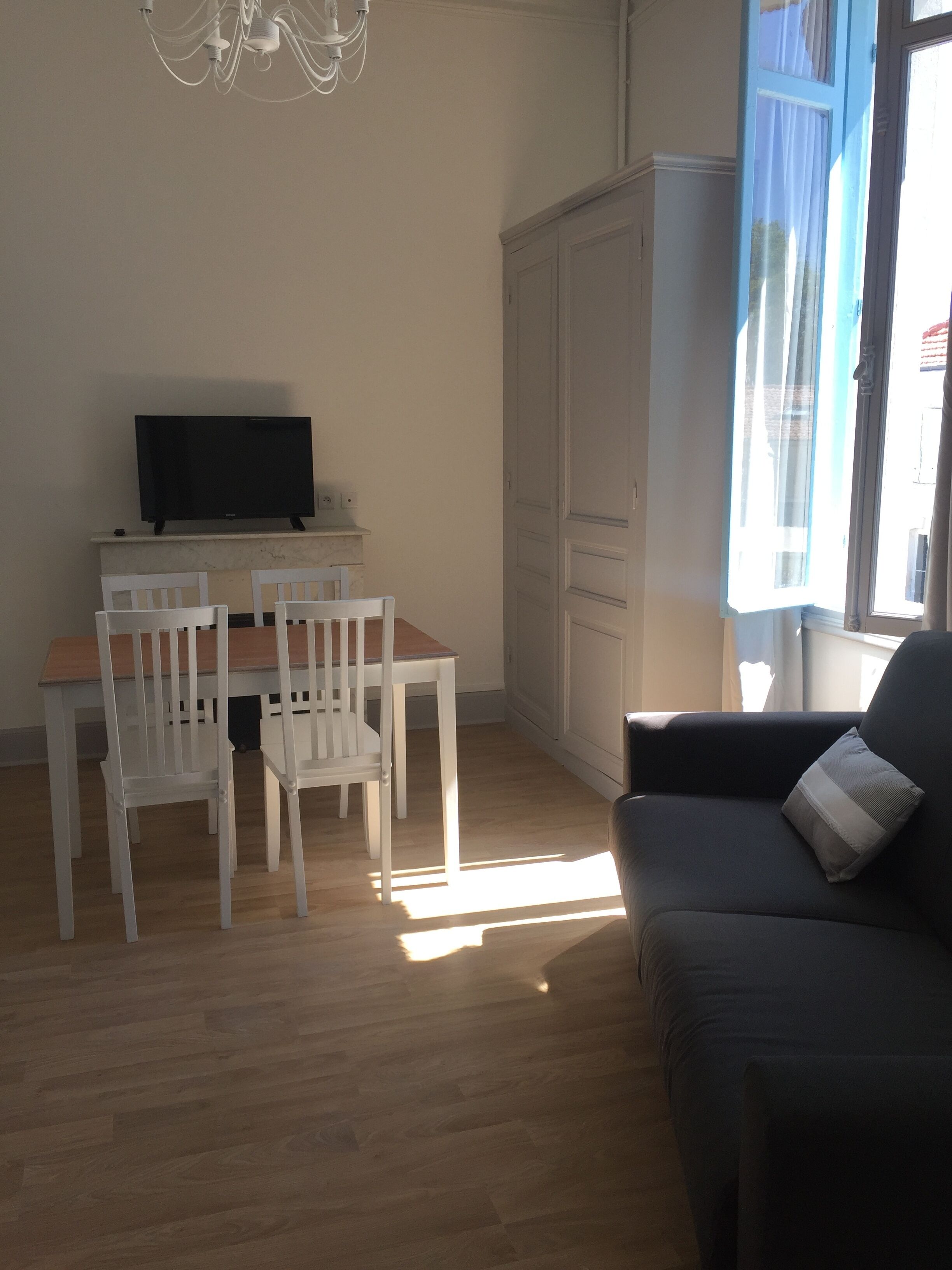 A living room with a sofa, a TV on a stand, a dining table with chairs, and a wardrobe.