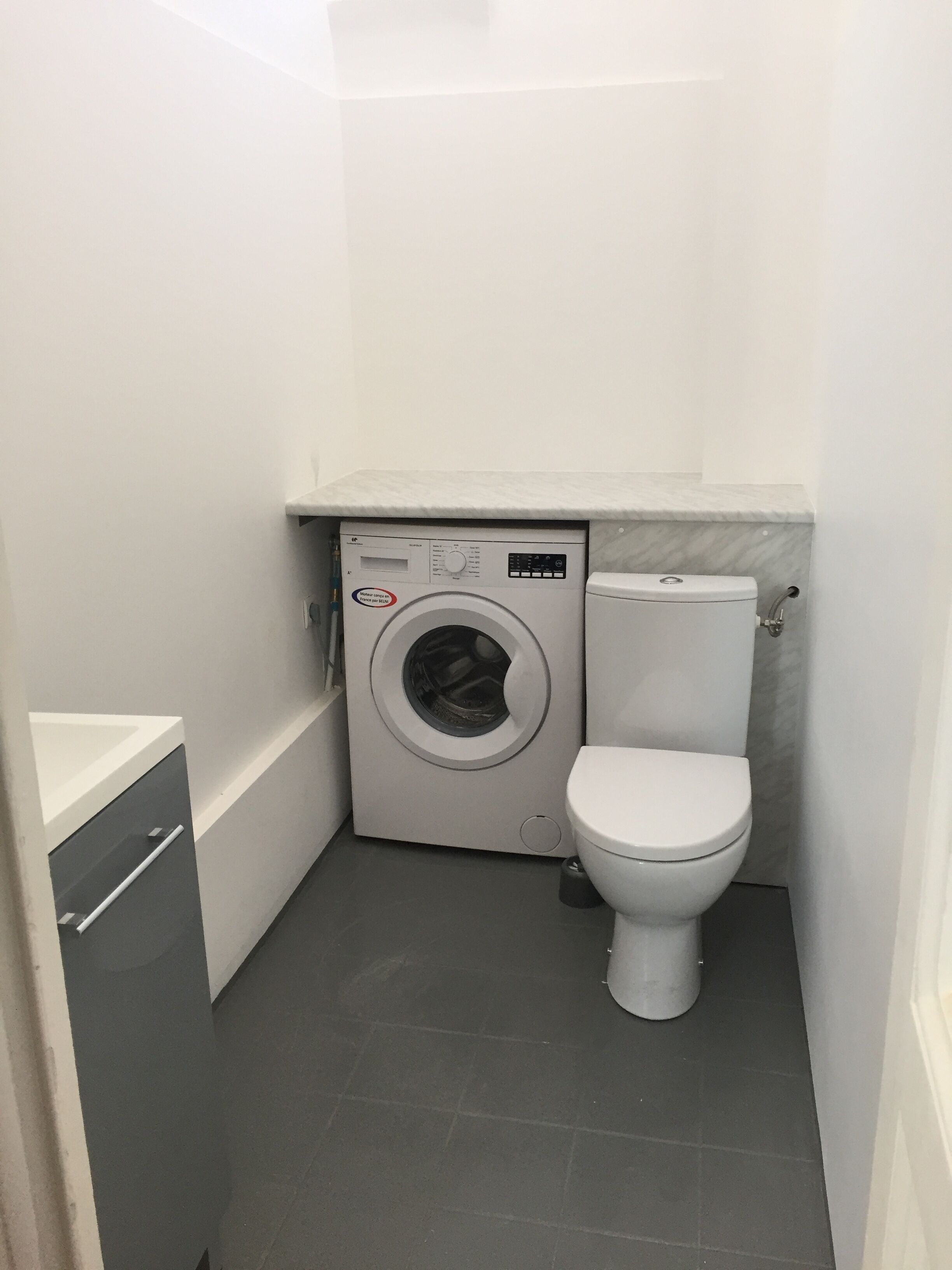 Un baño pequeño con lavadora, inodoro y un mueble auxiliar.