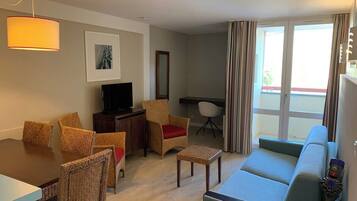 A living room with a dining table, chairs, a sofa, a TV, and a window with curtains.