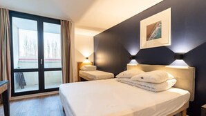 Une chambre d’hôtel avec un grand lit, deux tables de chevet, une fenêtre avec des rideaux et un tableau au mur.