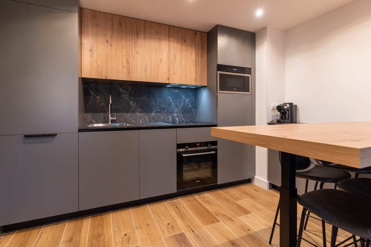 Une cuisine moderne avec des meubles gris, un plan de travail en bois, un four encastré et une machine à café.