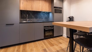 Une cuisine moderne avec des meubles gris, un plan de travail en bois, un four encastré et une machine à café.