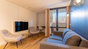 Un salon moderne avec un canapé, deux fauteuils, un téléviseur et une petite table.