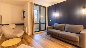 Un salon comprenant un canapé, un fauteuil et une petite table. Une porte-fenêtre coulissante donne accès à un balcon.
