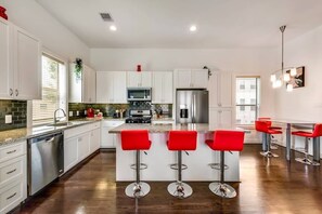 Enjoy cooking in this well-lit kitchen with a central island, bar stools, stainless steel appliances, and white cabinetry.