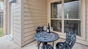 Eine Terrasse mit rundem Tisch und Stühlen, einer Weinflasche und einem Fenster mit Jalousien.