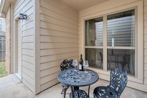 A patio with a round table and chairs, a bottle of wine, and a window with blinds.