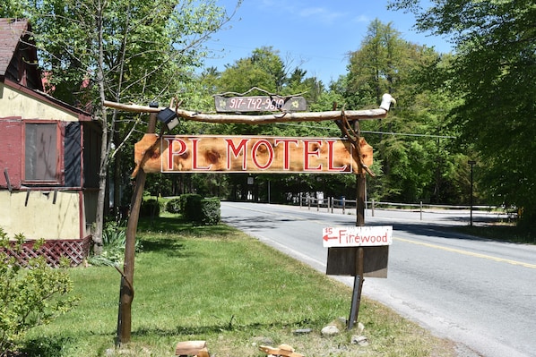 A rustic motel sign with a contact number and a directional sign for Firewood.