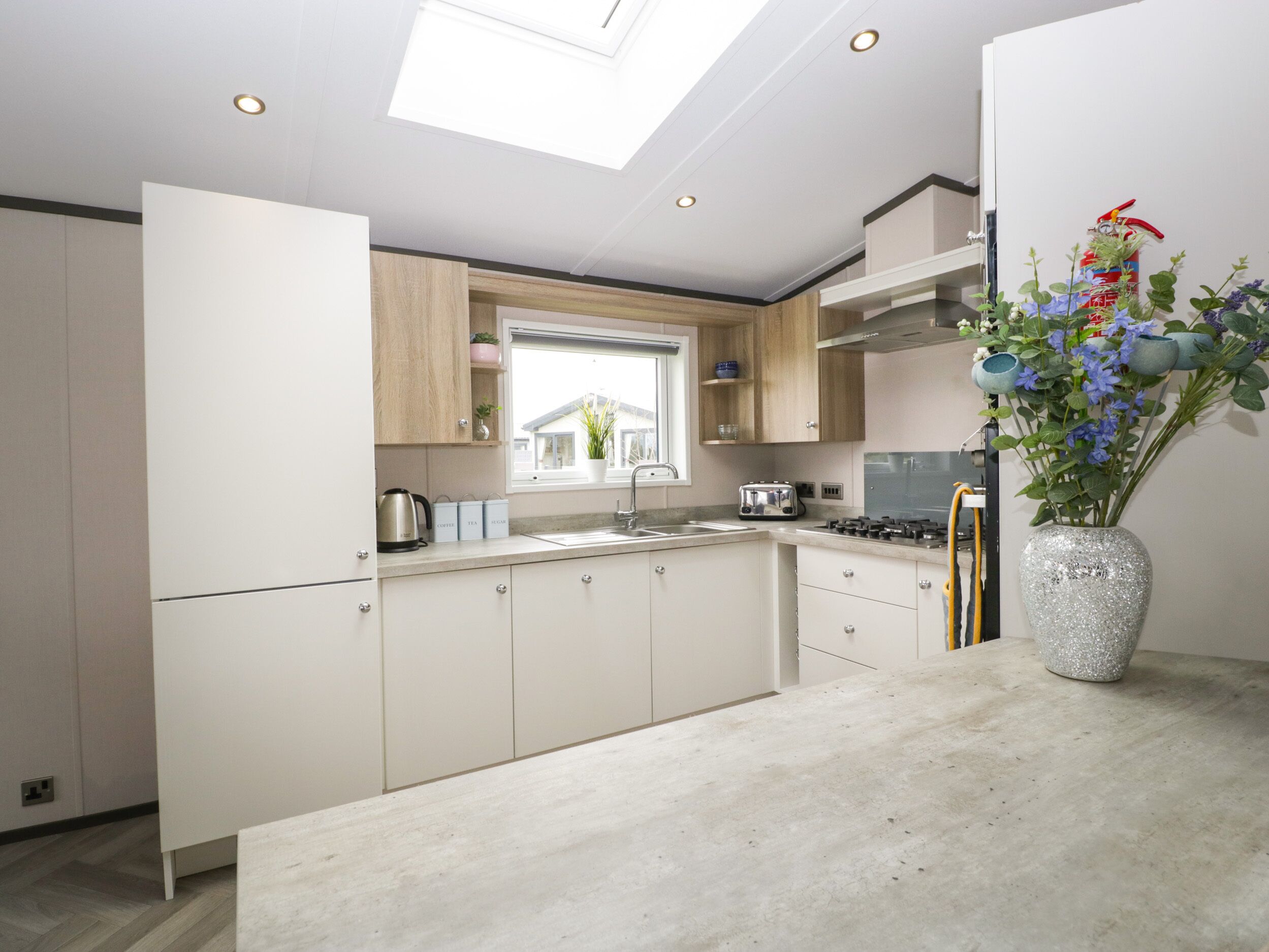A modern kitchen with a skylight, white cabinets, a stainless steel toaster, and a decorative vase with flowers.