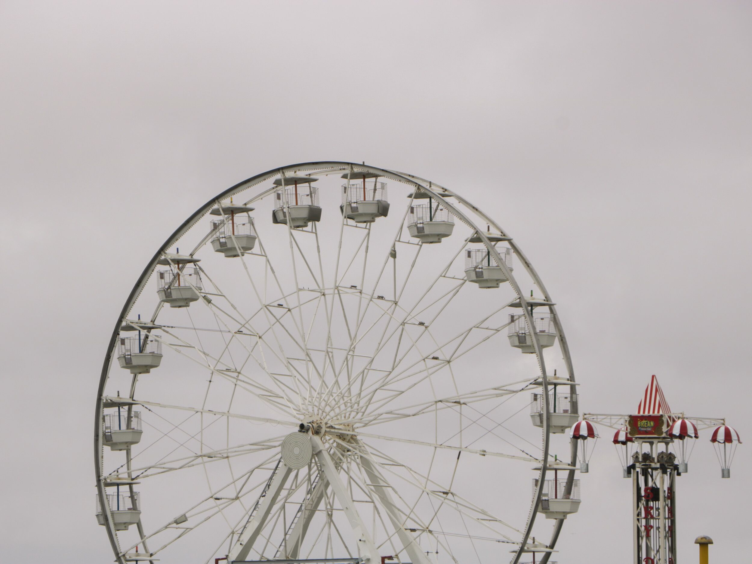 Une grande roue avec des cabines, une attraction plus petite dotée de parasols rouges et blancs à rayures, et une enseigne sur laquelle on peut lire « BREAN ».
