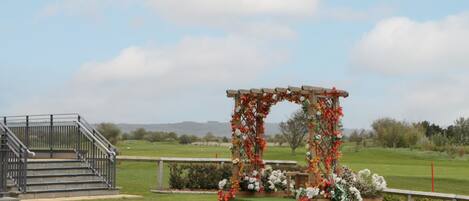 A wooden archway adorned with flowers, a staircase, and a grassy field with distant hills.