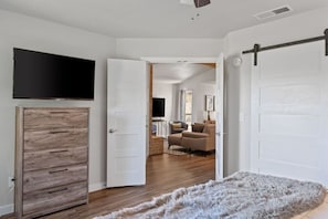 Ein Zimmer mit einem Holzschrank, einem flachbildfernseher an der Wand, einem flauschigen Teppich und einer Schiebetür im Bauernhausstil.