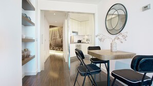 Une cuisine moderne avec des meubles blancs, une table à manger avec deux chaises et un miroir décoratif au mur.