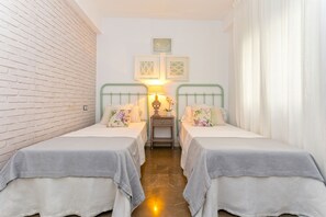 Une chambre avec deux lits, un mur en briques, une table de chevet avec une lampe et des œuvres d’art encadrées accrochées au mur.