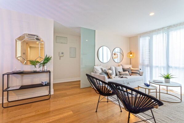 A modern living room with a sofa, two black chairs, a coffee table, a side table, a mirror, and a potted plant.
