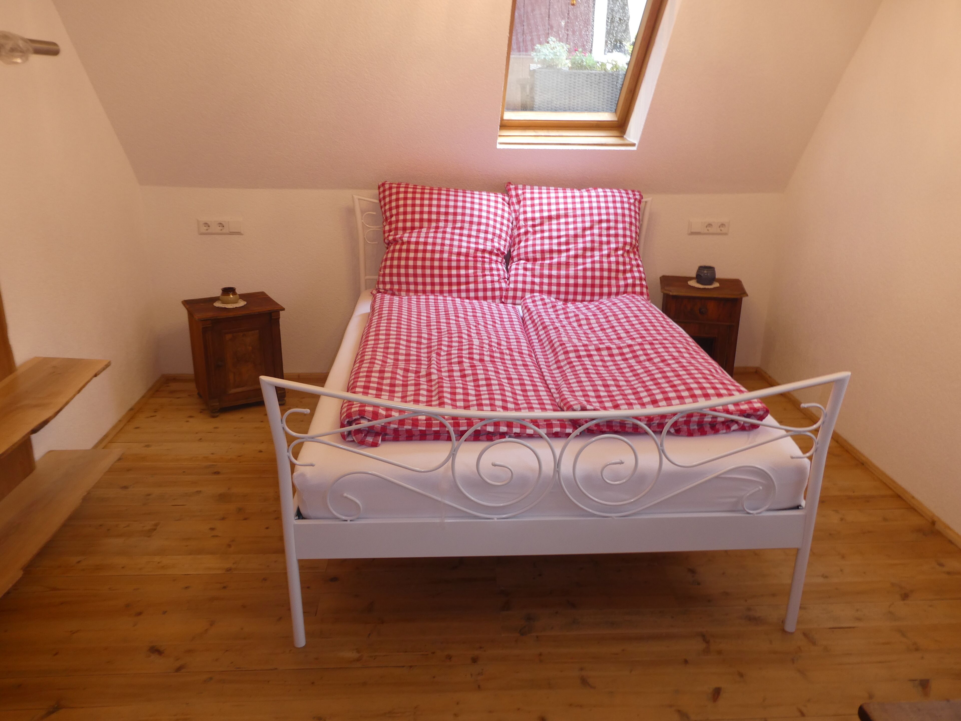 A small bedroom with a single bed, a wooden floor, a skylight, and a small bedside table.