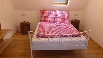 A small bedroom with a single bed, a wooden floor, a skylight, and a small bedside table.