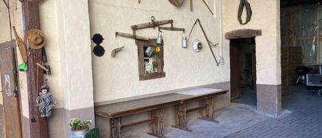 A rustic interior with a wooden bench, a small window with a flower, and various tools hanging on the wall.