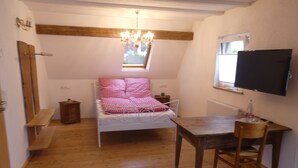 A small, cozy room with a bed, a wooden table, a chair, a small bedside table, a mirror, and a TV mounted on the wall. - s' Moose Hof (Weisweil)