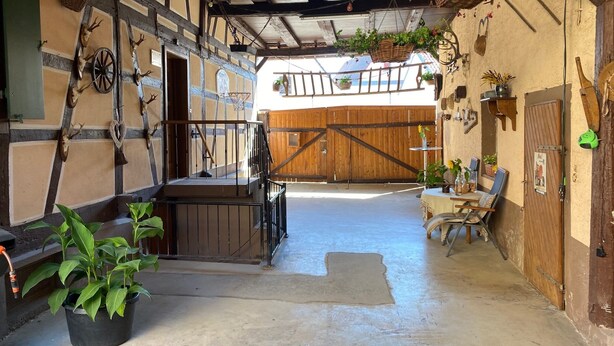 A rustic barn interior with a wooden staircase, hanging baskets, and a table with chairs. - s' Moose Hof (Weisweil)