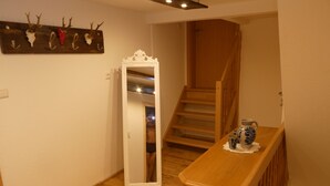 A wooden staircase leading to a second floor, a wooden bench with a vase and mug, and a wall-mounted mirror with antlers and a skull decoration. - s' Moose Hof (Weisweil)