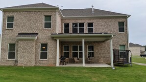 A two-story house with a covered patio area, a brick exterior, and a lawn in front. - Spacious 5BR 4BA Retreat: The Best Kept Secret in Covington (Covington)
