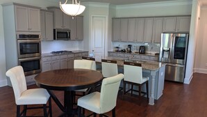 A modern kitchen with grey cabinets, stainless steel appliances, a round dining table with chairs, and a chandelier. - Spacious 5BR 4BA Retreat: The Best Kept Secret in Covington (Covington)