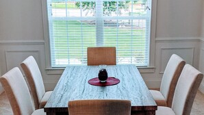 A dining room with a rectangular table, four upholstered chairs, a chandelier, and a window with blinds. - Spacious 5BR 4BA Retreat: The Best Kept Secret in Covington (Covington)