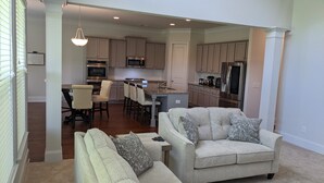 A modern kitchen with stainless steel appliances, a dining area with bar stools, and a living room with a sofa and patterned cushions. - Spacious 5BR 4BA Retreat: The Best Kept Secret in Covington (Covington)