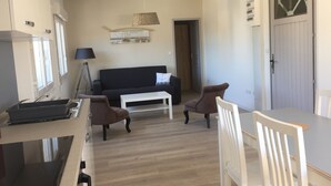 A modern living room with a black sofa, two brown armchairs, a white coffee table, and a kitchen area with a stove and sink. - Suite**** in charming 19th century residence with park and heated swimming pool (Arvert)