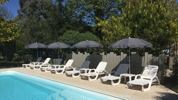 A swimming pool with white lounge chairs and umbrellas, surrounded by a wooden fence and trees. - Suite**** in charming 19th century residence with park and heated swimming pool (Arvert)