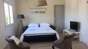 A bedroom with a bed, two armchairs, a desk with a TV, a lamp, and a painting on the wall. - Suite**** in charming 19th century residence with park and heated swimming pool (Arvert)