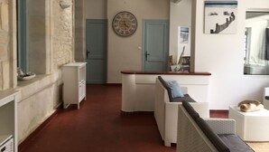 A hallway with a stone wall, a clock, a door, and a seating area with cushions. - Suite**** in charming 19th century residence with park and heated swimming pool (Arvert)