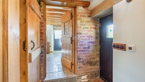 A wooden door leading to a hallway with a brick wall and a black door.