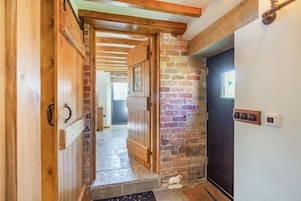 Una puerta de madera que da a un pasillo con pared de ladrillo y una puerta negra.