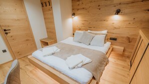 Camera da letto con rivestimento in legno, un letto, comodini e una sedia.