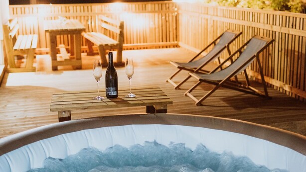 Una vasca idromassaggio con due poltrone relax e una bottiglia di vino su un pontile di legno.